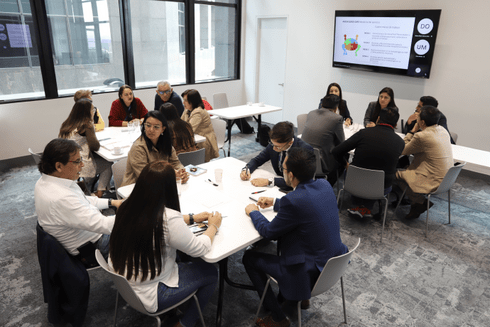 Group of men and women seated in tables of four, participating in a training session in a classroom-style setting - IDB - Inter-American Development Bank - Knowledge for Development